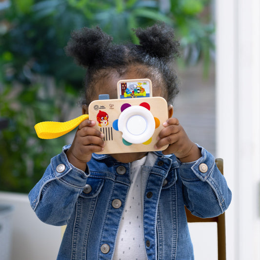 una niña jugando con la camara fotografica, un juguete infantil que aparenta ser una camara de fotos de madera que al girar el lente se seleccionan colores que la camara puede decir en 5 idiomas distintos