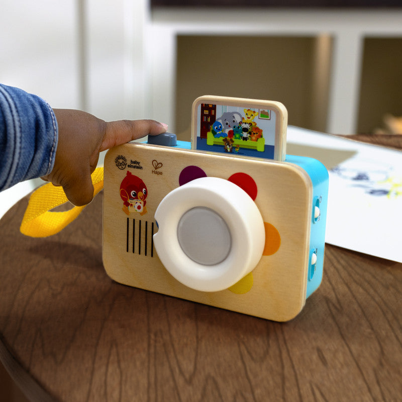 la camara fotografica baby einstein en una mesa con un dedo apretando el boton de disparo 